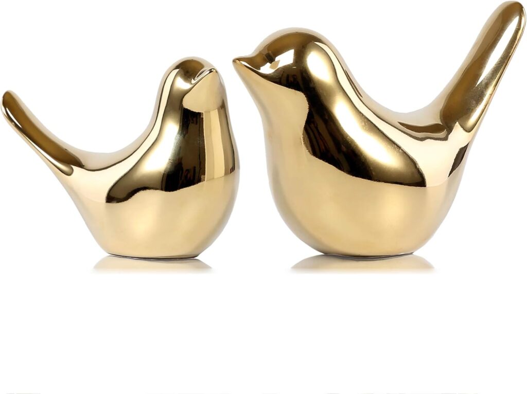 Two small, polished gold bird figurines used as decorative accents on top of a stack of books.